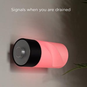 May include: A cylindrical, battery-shaped lamp with a black top and a gray end. The lamp glows red, with the text "Signals when you are drained" above it. The lamp is mounted on a light gray wall.