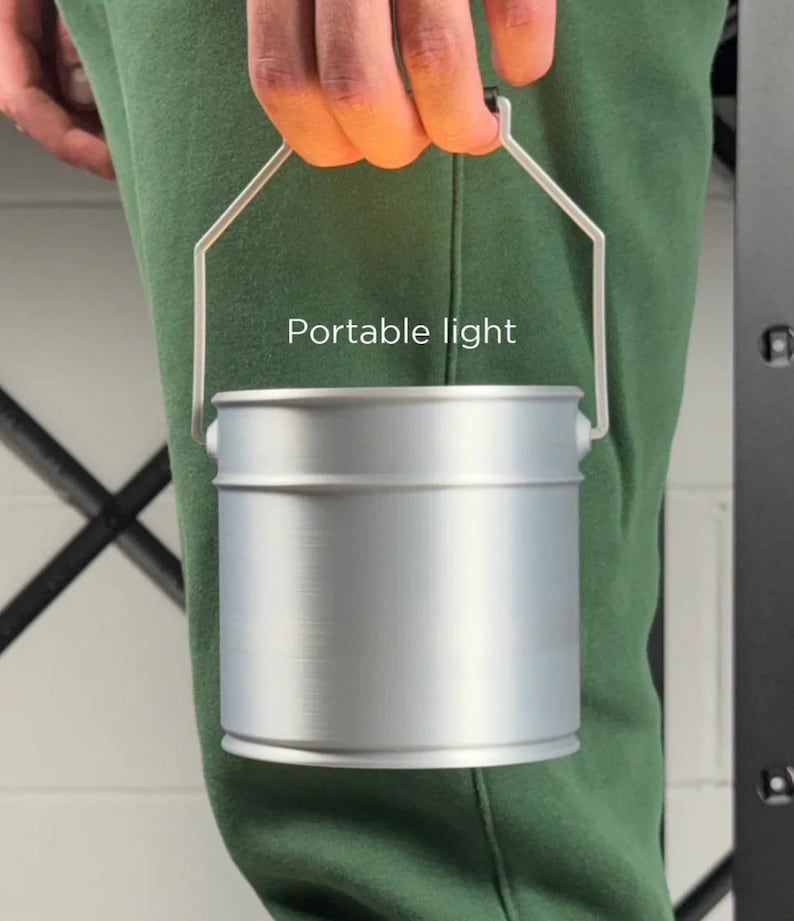 May include: A silver-colored portable light with a handle. The cylindrical light has a handle made of thin metal. The text "Portable light" is printed on the front of the light.