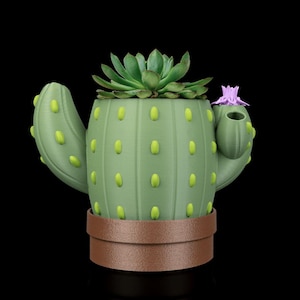 May include: A green cactus-shaped plant pot with a brown base and yellow accents. It contains a green succulent and a small purple flower. This decorative pot is a unique way to display plants.