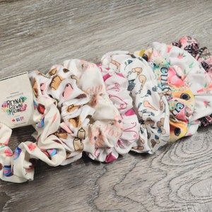 May include: A set of six colorful scrunchies with various patterns, including a flamingo, a floral design, and a geometric pattern. The scrunchies are made of soft fabric and are perfect for holding hair in place.