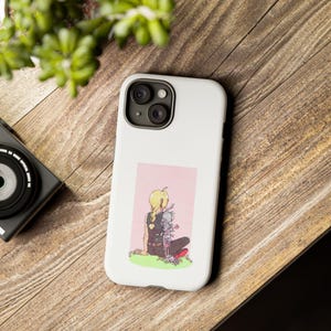 May include: A white phone case with a pink background image of a blonde anime character with a mechanical arm. The character is sitting on a patch of grass with flowers.