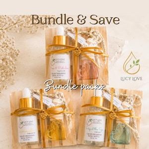 May include: Three car air freshener gift sets by Lucy Love, each featuring a 15ml refill bottle and a heart-shaped glass diffuser with a hanging cord, tied with gold ribbon on a wooden base. Labels read Rose & Pistachio, Limoncello, and Day at the Spa.