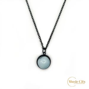 Puede incluir: Un collar de cadena negra con un colgante redondo con un diseño de vidrio marmoleado azul claro y blanco.