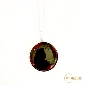 May include: A silver chain necklace with a round, dark red pendant. The pendant is made of glass and has a reflective surface.