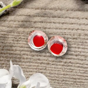 Op de afbeelding: Twee rode glazen ogen met een heldere plastic omhulling rond de rode iris. De ogen liggen op een houten oppervlak.
