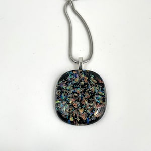 May include: A silver chain necklace with a black glass pendant. The pendant has a speckled pattern of iridescent blue, green, and gold.