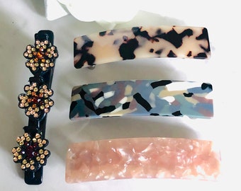 May include: Set of four hair clips with different patterns. The clips are made of a tortoiseshell-like material and have a curved shape. The clips are in various colors, including brown, black, white, gray, and pink.
