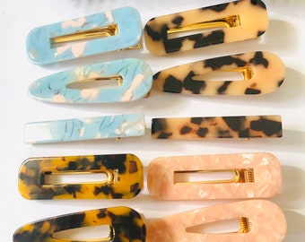 May include: Set of ten hair clips in various colors and patterns. The clips are made of plastic and have a gold metal clasp. The patterns include tortoise shell, blue and white marble, and pink and white marble.