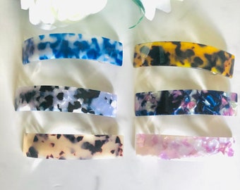 May include: Six tortoise shell hair clips in different colors, including blue, black, white, yellow, pink, and purple. The clips are made of a hard plastic material and have a curved shape.
