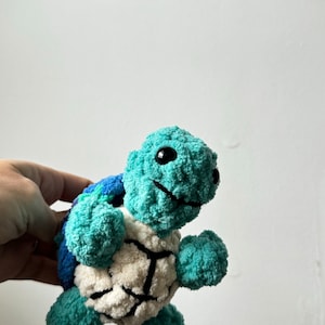 May include: A teal blue and white crocheted stuffed turtle toy with black eyes.