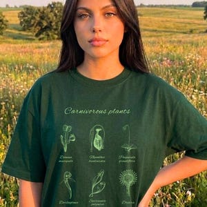 May include: Dark green t-shirt featuring the text "Carnivorous plants" and botanical illustrations of various carnivorous plants. The shirt includes the names of the plants. The Garrison Trend logo is in the bottom right corner.