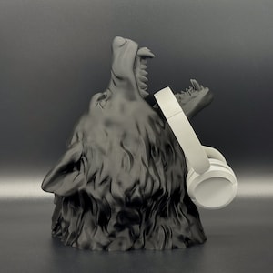 Könnte beinhalten: Eine schwarze, 3D-gedruckte Wolfskopfskulptur mit offenem Maul, die einen weißen kabellosen Kopfhörer hält.