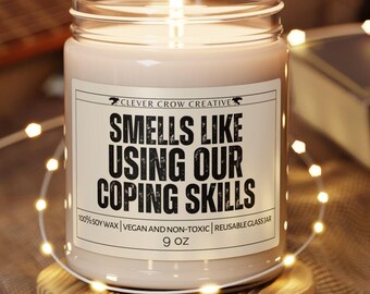 以下が含まれることがあります： 「Smells Like Using Our Coping Skills」と書かれたラベルが付いたガラス瓶に入った、火の灯ったキャンドル。 キャンドルは小さな木製のコースターの上にあります。 キャンドルは255グラムです。
