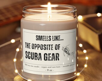 May include: A brown soy wax candle in a clear glass jar with a white label that reads "Smells Like... The Opposite of Scuba Gear". The candle is lit and sitting on a wooden coaster.