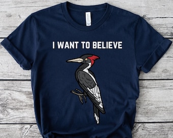 May include: A navy blue t-shirt with a white woodpecker illustration and the text "I WANT TO BELIEVE".