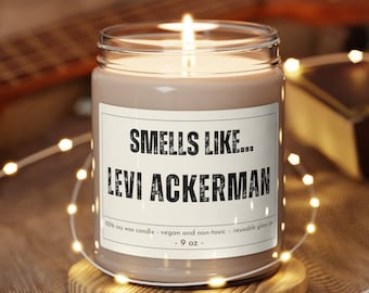 May include: A brown soy wax candle in a clear glass jar with a white label that reads "Smells Like... Levi Ackerman". The label also includes the text "100% soy wax candle - vegan and non-toxic - reusable glass jar - 9 oz."