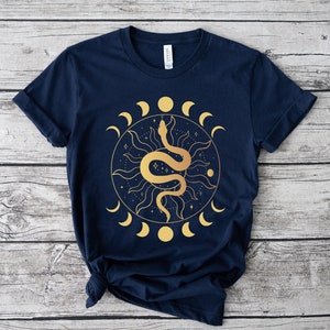 May include: A navy blue t-shirt with a gold graphic of a snake wrapped around a sun with a crescent moon design.