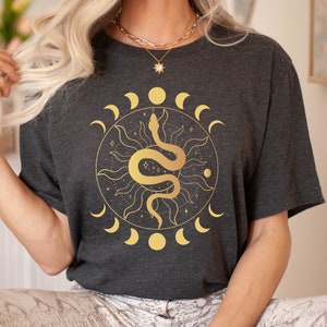 May include: A dark gray t-shirt with a gold graphic of a snake wrapped around a sun with a crescent moon design.