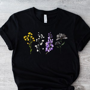 Puede incluir: Camiseta negra con un diseño floral con flores amarillas, blancas, moradas y grises.