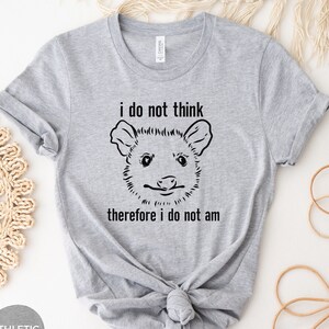 May include: A grey t-shirt with a black and white illustration of an opossum with the text "i do not think therefore i do not am"