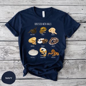 May include: Navy blue t-shirt with the text "OBSESSED WITH BALLS" and illustrations of various snake morphs. The shirt features a crew neck and short sleeves. The color of the shirt is navy.