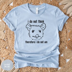 May include: Light blue t-shirt featuring a black and white illustration of an opossum and the text "i do not think therefore i do not am"