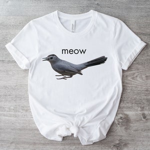 May include: White t-shirt with a gray bird graphic and the word "meow" printed in black.