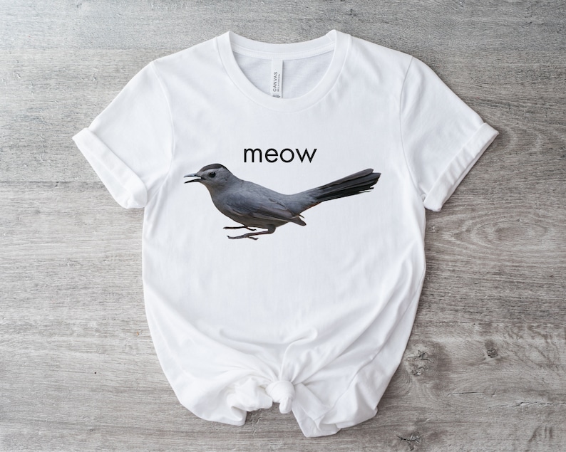 May include: White t-shirt with a gray bird graphic and the word "meow" printed in black.
