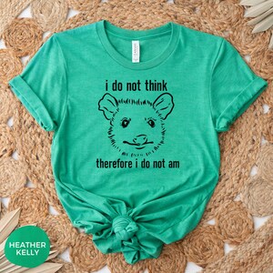 May include: A green t-shirt featuring a black and white illustration of an opossum and the text "i do not think therefore i do not am"