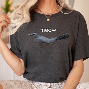 May include: A dark gray t-shirt with a gray bird graphic and the word "meow" printed on the front.