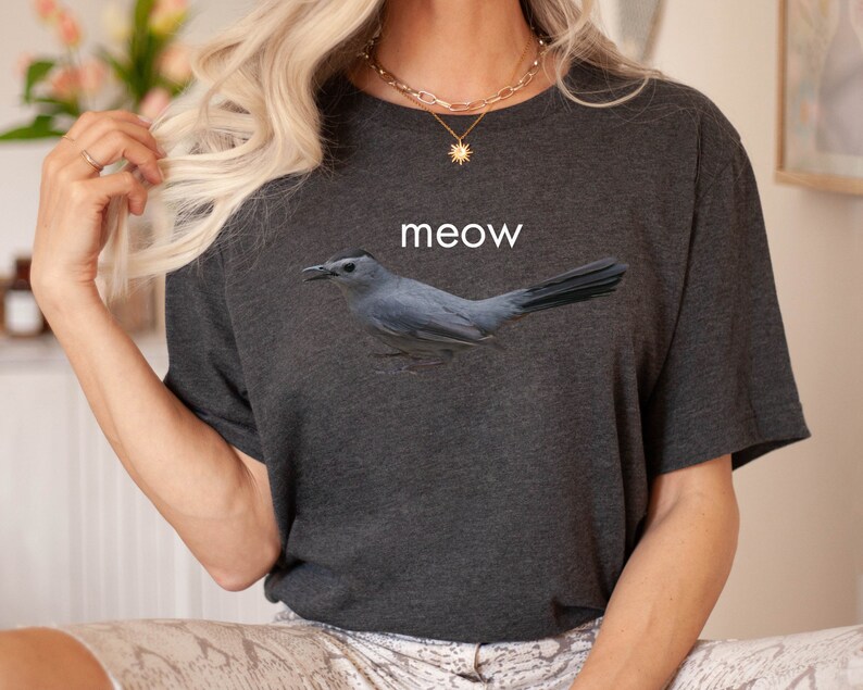 May include: A dark gray t-shirt with a gray bird graphic and the word "meow" printed on the front.