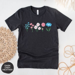 May include: A dark heather grey t-shirt with a row of colorful flowers printed on the front. The flowers are blue, pink, and white.