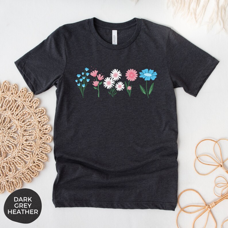 May include: A dark heather grey t-shirt with a row of colorful flowers printed on the front. The flowers are blue, pink, and white.