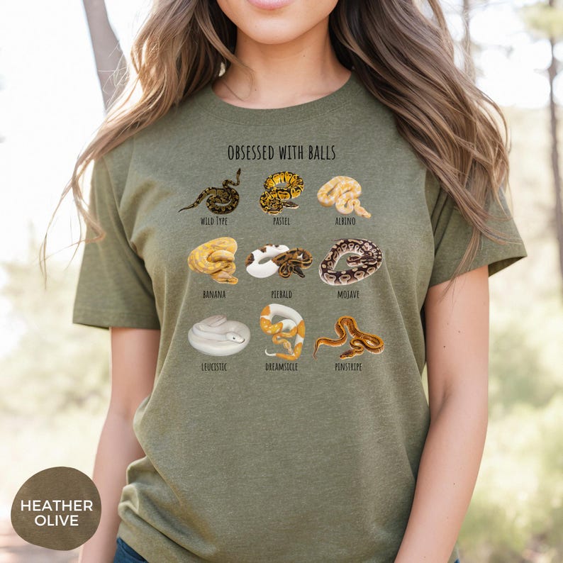 May include: Heather olive green t-shirt with the text "OBSESSED WITH BALLS" and illustrations of various snake morphs. The shirt features a round neck and short sleeves. The bottom left corner of the shirt has the text "HEATHER OLIVE".