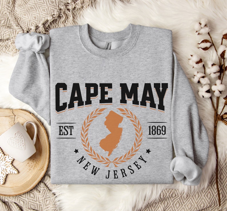 May include: Gray sweatshirt with a black and orange graphic design. The graphic features the text "CAPE MAY EST 1869 NEW JERSEY" with a laurel wreath and an outline of the state of New Jersey.