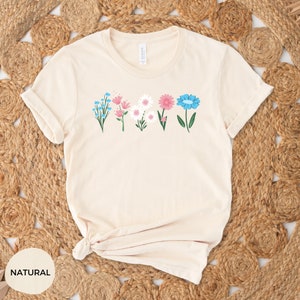 May include: A beige t-shirt with a row of five colorful flowers printed on the front. The flowers are blue, pink, white, and green.