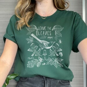 May include: A dark green t-shirt with a white graphic design featuring a bird, leaves, and the text "Leave the Leaves".