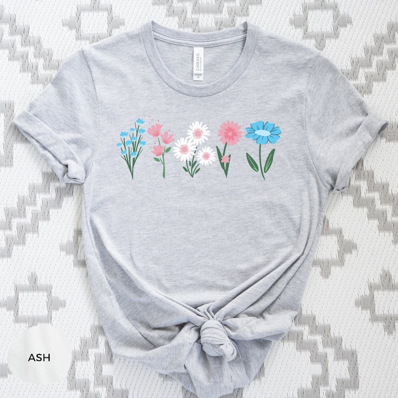 May include: A gray t-shirt with a row of five colorful flowers printed on the front. The flowers are blue, pink, white, and green.