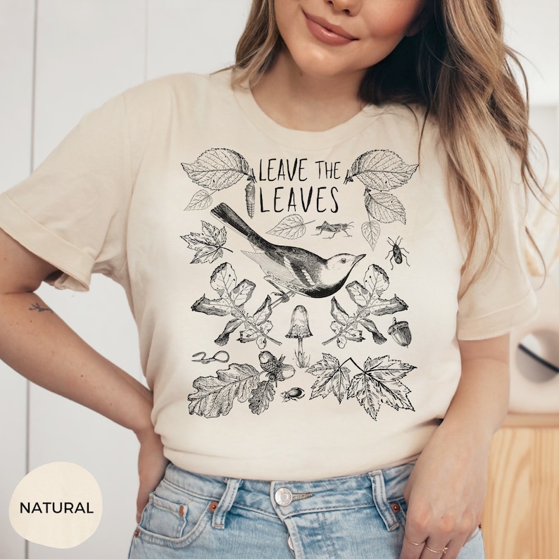 May include: A beige t-shirt with a black and white illustration of a bird, leaves, and acorns. The text "LEAVE THE LEAVES" is printed on the shirt.