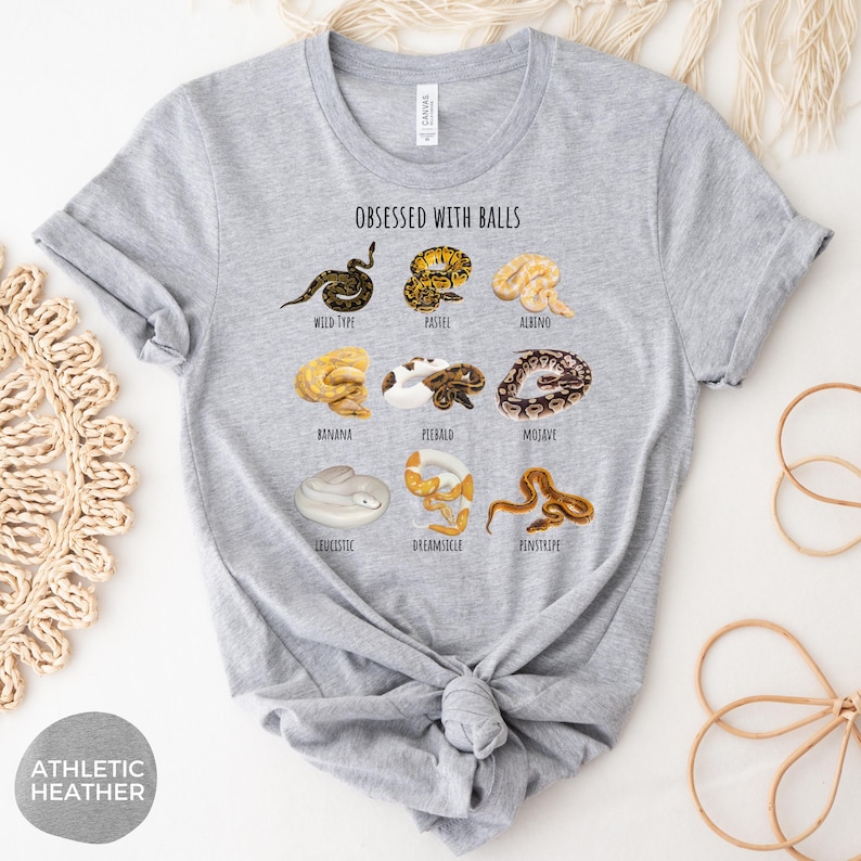 May include: Athletic heather gray t-shirt with the text "OBSESSED WITH BALLS" and illustrations of various snake morphs. The shirt features a crew neck and short sleeves. The snake morphs include Wild Type, Pastel, Albino, Banana, Piebald, Mojave, Leucistic, Dreamsicle, and Pinstripe.