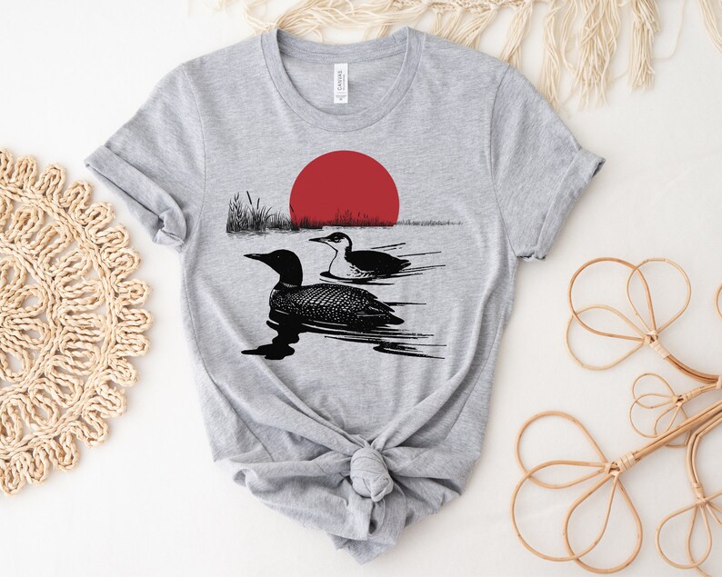 May include: Gray t-shirt with a black and white illustration of two loons swimming in a lake with a red sun setting in the background.