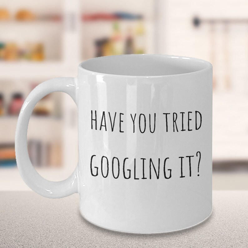 K&ouml;nnte beinhalten: Wei&szlig;e Keramik-Kaffeetasse mit schwarzem Text, der "Hast du es schon mal gegoogelt?" lautet.
