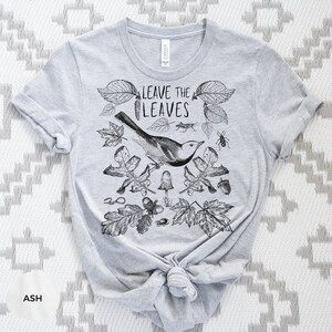 May include: A gray t-shirt with a black and white illustration of leaves, a bird, and insects. The text "Leave the Leaves" is printed on the shirt.
