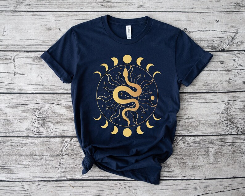 May include: A navy blue t-shirt with a gold graphic of a snake wrapped around a sun with a crescent moon design.