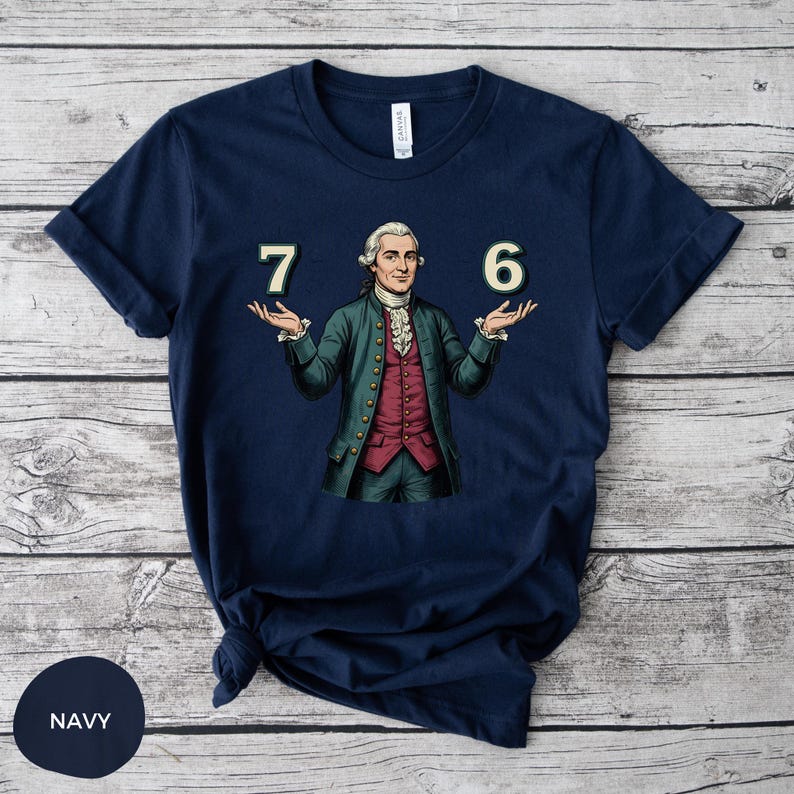 May include: Navy blue t-shirt featuring a historical figure with the numbers "7" and "6" on either side. The figure is dressed in a green coat, red vest, and white cravat. The shirt is made of a soft material.