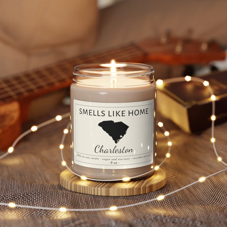 Peut inclure: Une bougie en cire de soja brune dans un pot en verre transparent avec une &eacute;tiquette blanche qui indique "Smells Like Home" et pr&eacute;sente une silhouette noire de l'&eacute;tat de Caroline du Sud. L'&eacute;tiquette indique &eacute;galement "Charleston" et "100% bougie en cire de soja - v&eacute;g&eacute;talienne et non toxique - pot en verre r&eacute;utilisable - 9 oz."