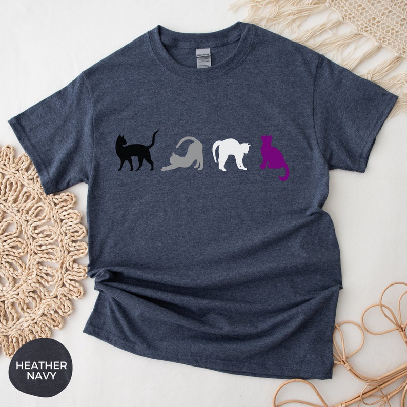May include: A heather navy blue t-shirt with a row of four cats in black, gray, white, and purple, representing the asexual pride flag.
