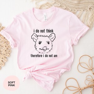 May include: A soft pink t-shirt featuring a black and white illustration of an opossum and the text "i do not think therefore i do not am"