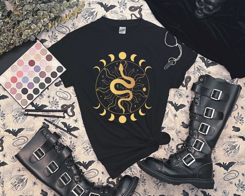 May include: Black t-shirt with a gold snake and moon design. The snake is coiled around a sun with a starburst pattern. The moon phases are around the sun and snake.