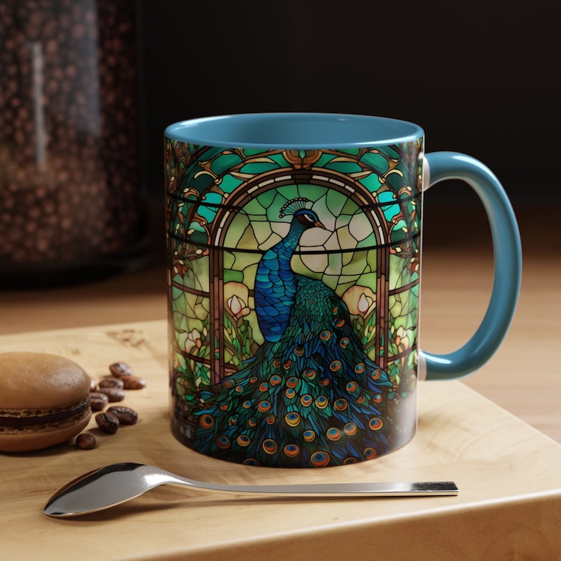 May include: A blue ceramic mug with a stained glass design of a peacock with a green and blue tail. The mug has a blue handle.